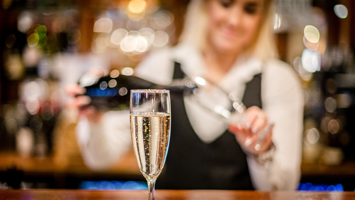 Ett glas champagne fylls av en leende servitris på Hotel Skansen. Bakgrunden är mjukt oskarp med glittrande ljus