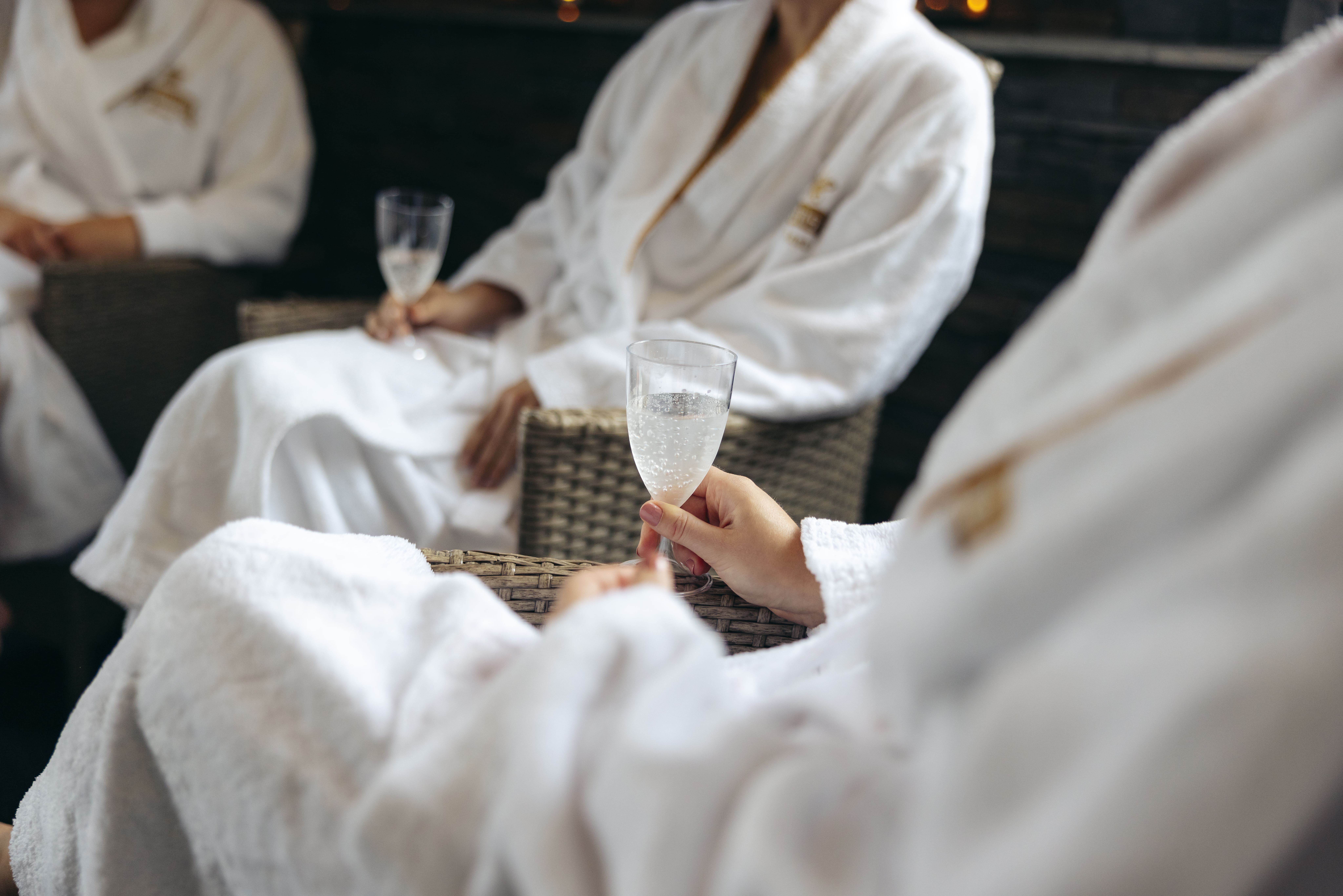 Gäster i vita morgonrockar på Hotel Skansen sitter avslappnade i flätade stolar och håller i glas med champagne, vilket skapar en känsla av lyx och avkoppling i en rofylld spa-miljö.