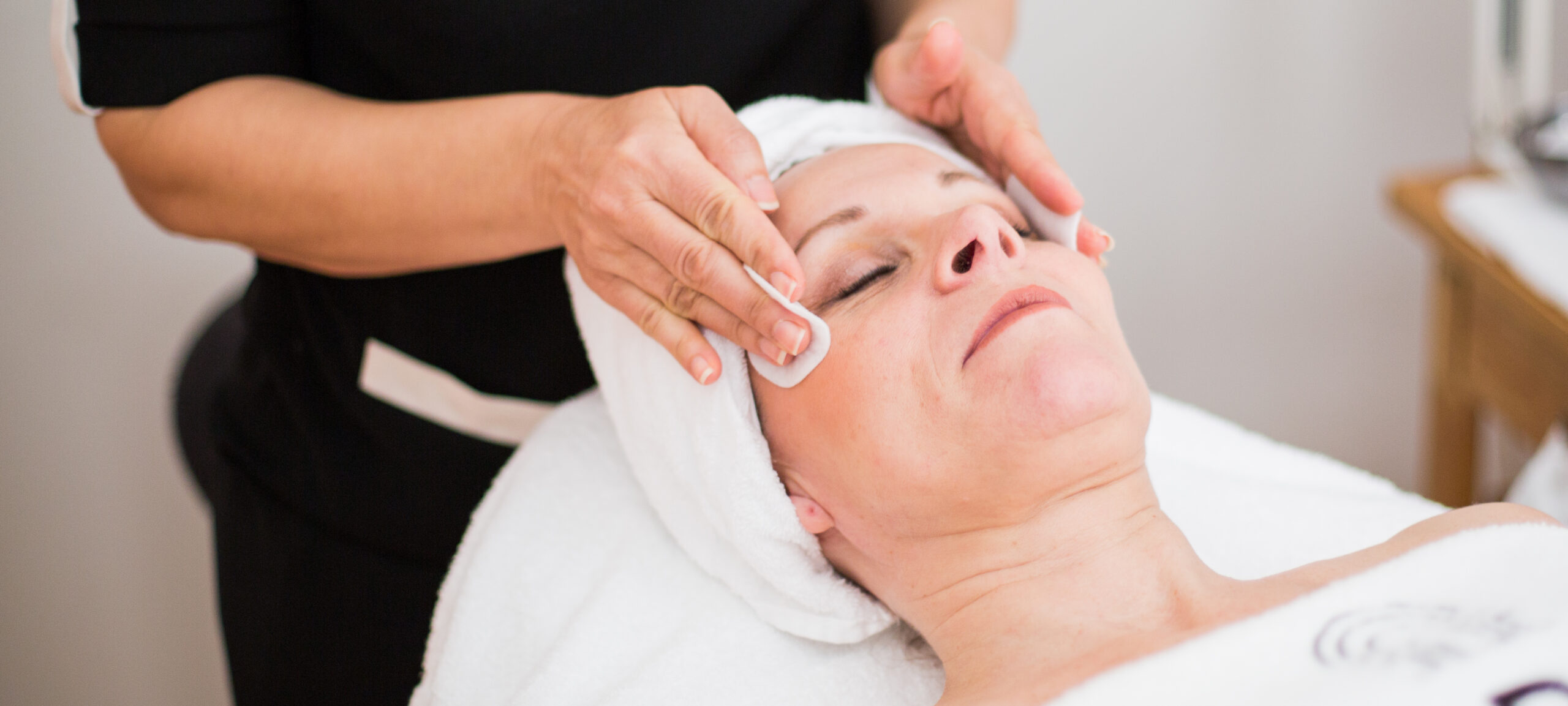 En gäst får en avslappnande ansiktsbehandling på Hotel Skansens spa, i en rofylld atmosfär med professionell omsorg.