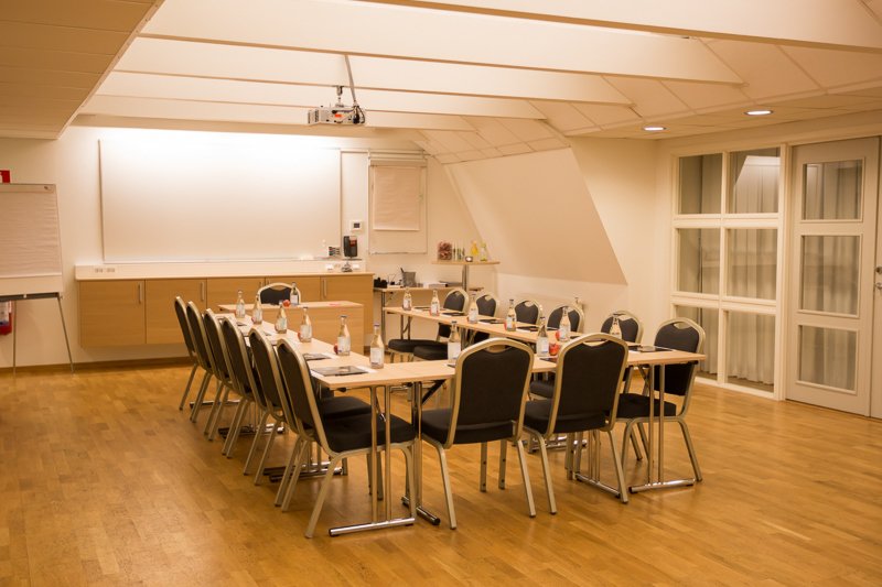 Ett modernt konferensrum med sluttande tak, u-bord och vattenflaskor, perfekt för kreativa möten på Hotel Skansen.