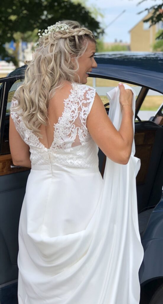 En klassisk vit bröllopsbil dekorerad med blommor, parkerad utanför Hotel Skansen, redo att föra brudparet till festligheterna.