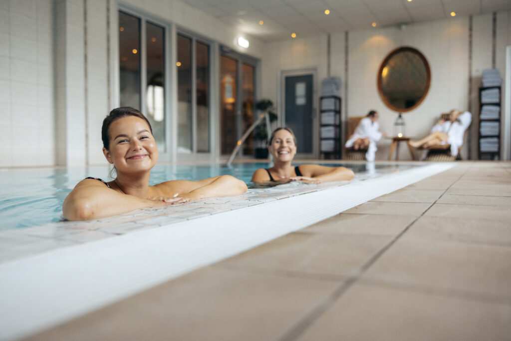 Två gäster njuter av en avslappnande stund i inomhuspoolen på Hotel Skansens spaavdelning.