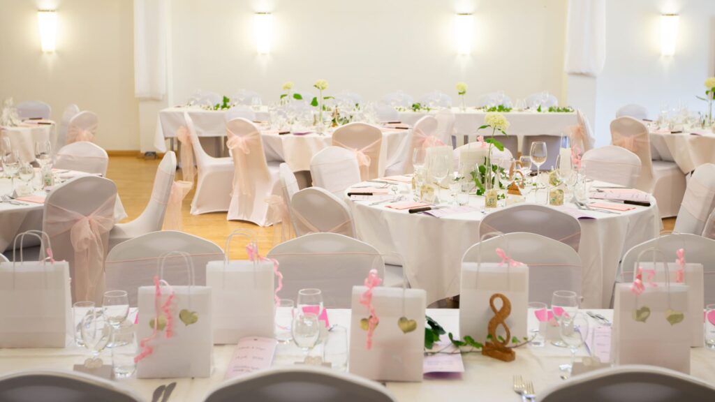 En festlig dukning med vita paket, rosa band och eleganta glas på runda bord, redo för bröllop på Hotel Skansen.