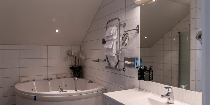 På bildens syns badrummet i en minisvit hos Hotel Skansen på Öland. I badrummet finns jacuzzi, dusch, toalett, handfat och spegel.