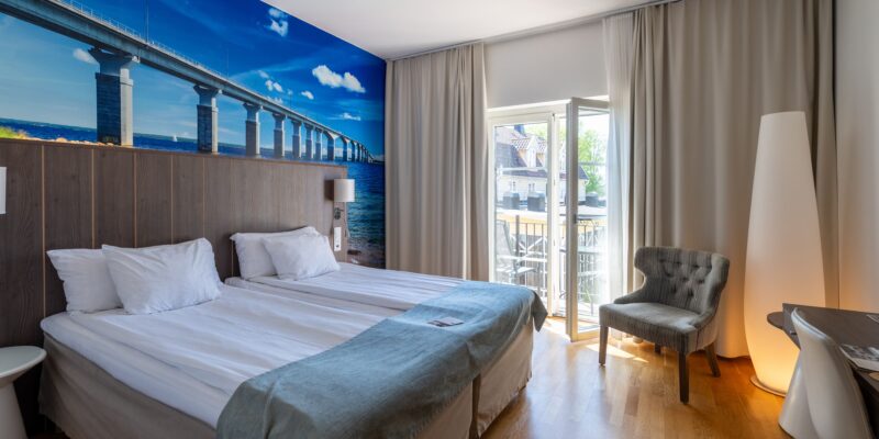 På bildens syns ett standardrum med uteplats hos Hotel Skansen på Öland. Rummet har en dubbelsäng och en öppnad dörr som leder ut till en balkong.