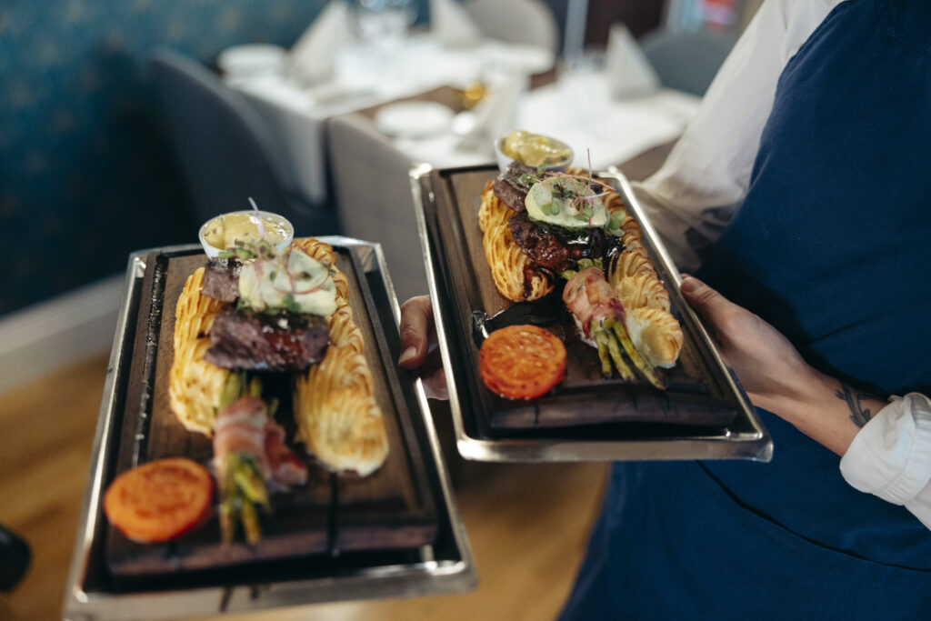 Två eleganta tallrikar med kött, duchessepotatis, bearnaisesås och garnering serveras på Hotel Skansen.