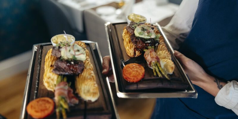 Två eleganta tallrikar med kött, duchessepotatis, bearnaisesås och garnering serveras på Hotel Skansen.