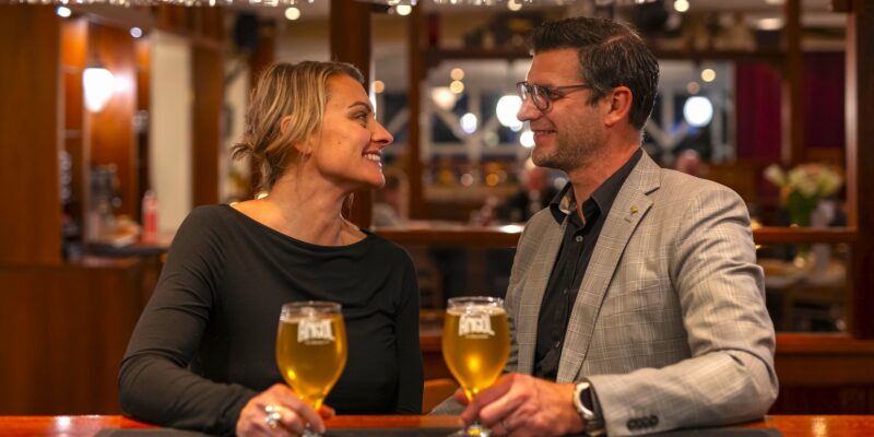 Ett par skålar och ler mot varandra över varsin öl i Hotel Skansens välkomnande bar.