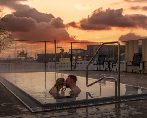 Ett par delar ett ögonblick i den ångande utomhuspoolen under en dramatisk solnedgång på Hotel Skansen.