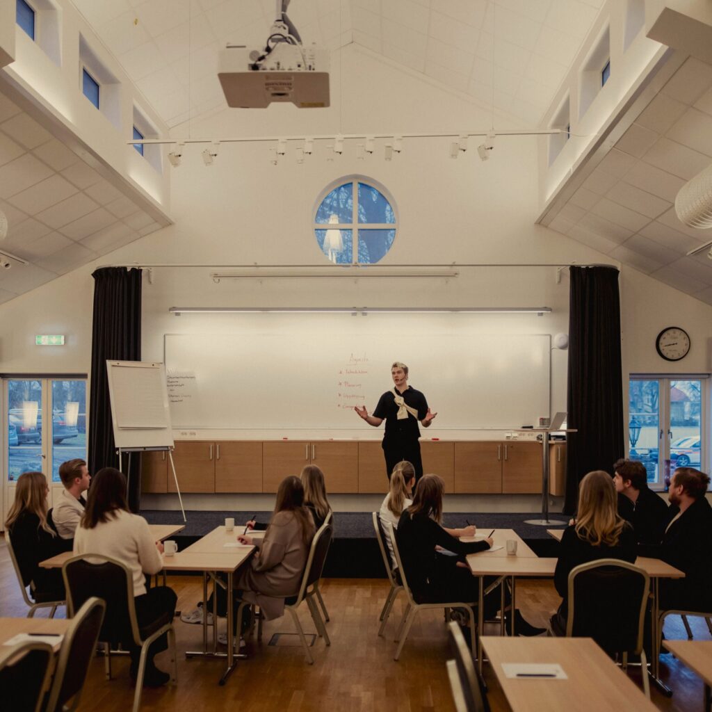 En föreläsare står framför en grupp deltagare i en ljus och rymlig konferenslokal på Hotel Skansen, med fokus på dialog och inspiration.