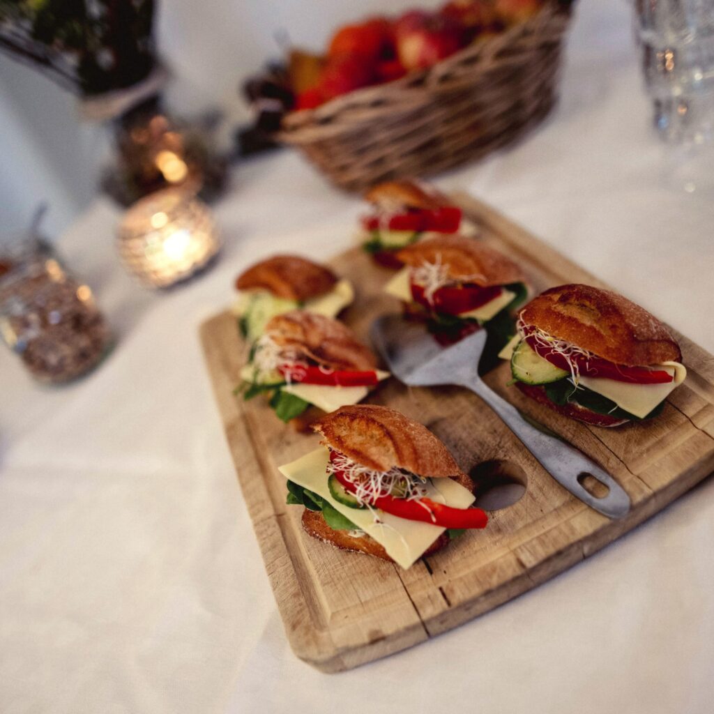 Små croissantmackor med färska grönsaker och ost på ett träfat, omgivna av ljuslyktor – en inbjudande fika på Hotel Skansen.