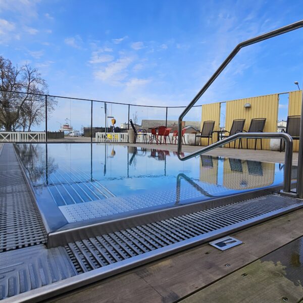 På bilden syns Hotel Skansens utomhuspool med räcke, ett stort trädäck, utomhusstolar med glasbord. Runt trädäcket finns ett glasstaket.