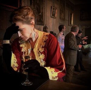 På bilden syns en kvinna hållandes att champangeglas. Kvinnan är iklädd en äldre stil och håller sig för pannan.