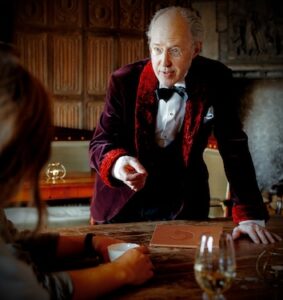 På bilden syns en man lutandes över ett skrivbord. Mannen är iklädd en sammetskostym och ser ut att intensivt diskutera något.