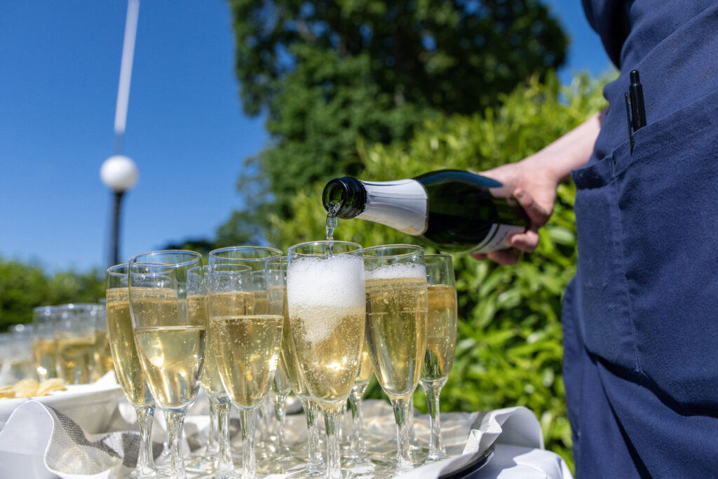 På bilden syns flera champangeglas fyllda med mousserande vin samt ett glas som håller på att fyllas med vin från en flaska hos Hotel Skansen