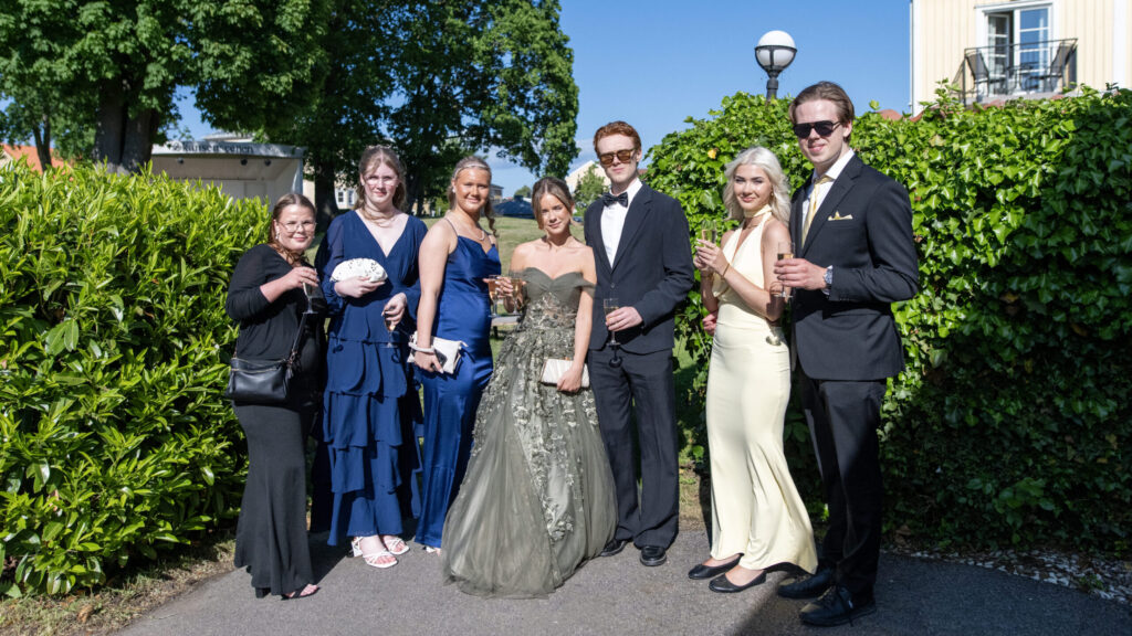 Bilden föreställer ett kompisgäng med killar och tjejer, klädda i klänningar och kostymer, hos Hotel Skansen påväg till sin studentbal.
